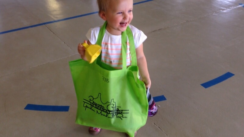 My kid wearing the race bag around her neck while holding a cowbell.