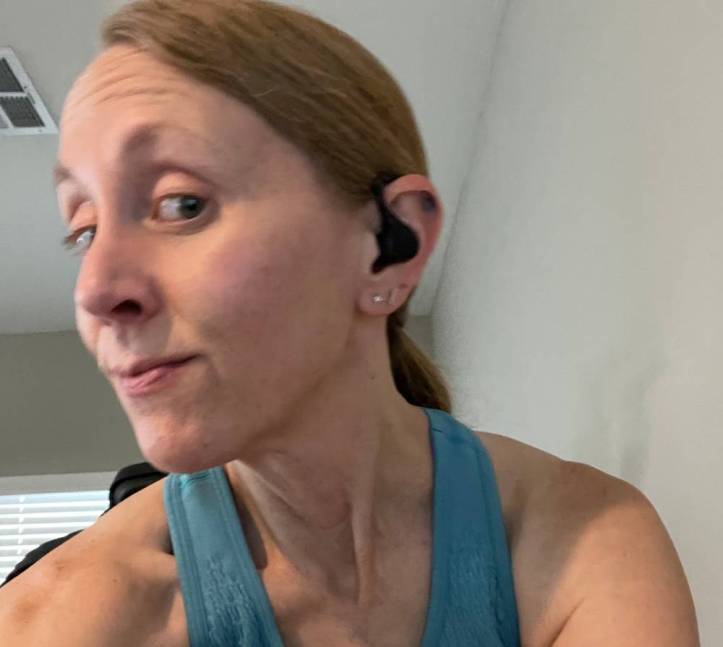 Blurry pic of Jill wearing the iLive wireless earbud on the bike indoors.